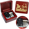 A red wooden music box with an open lid displaying a brass mechanism and a gold-colored box featuring The Godfather logo.