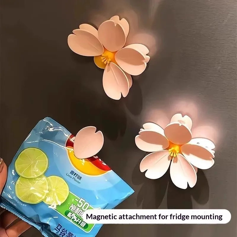 A light pink cherry blossom flower is shown next to a blue package for magnetic attachment for fridge mounting.