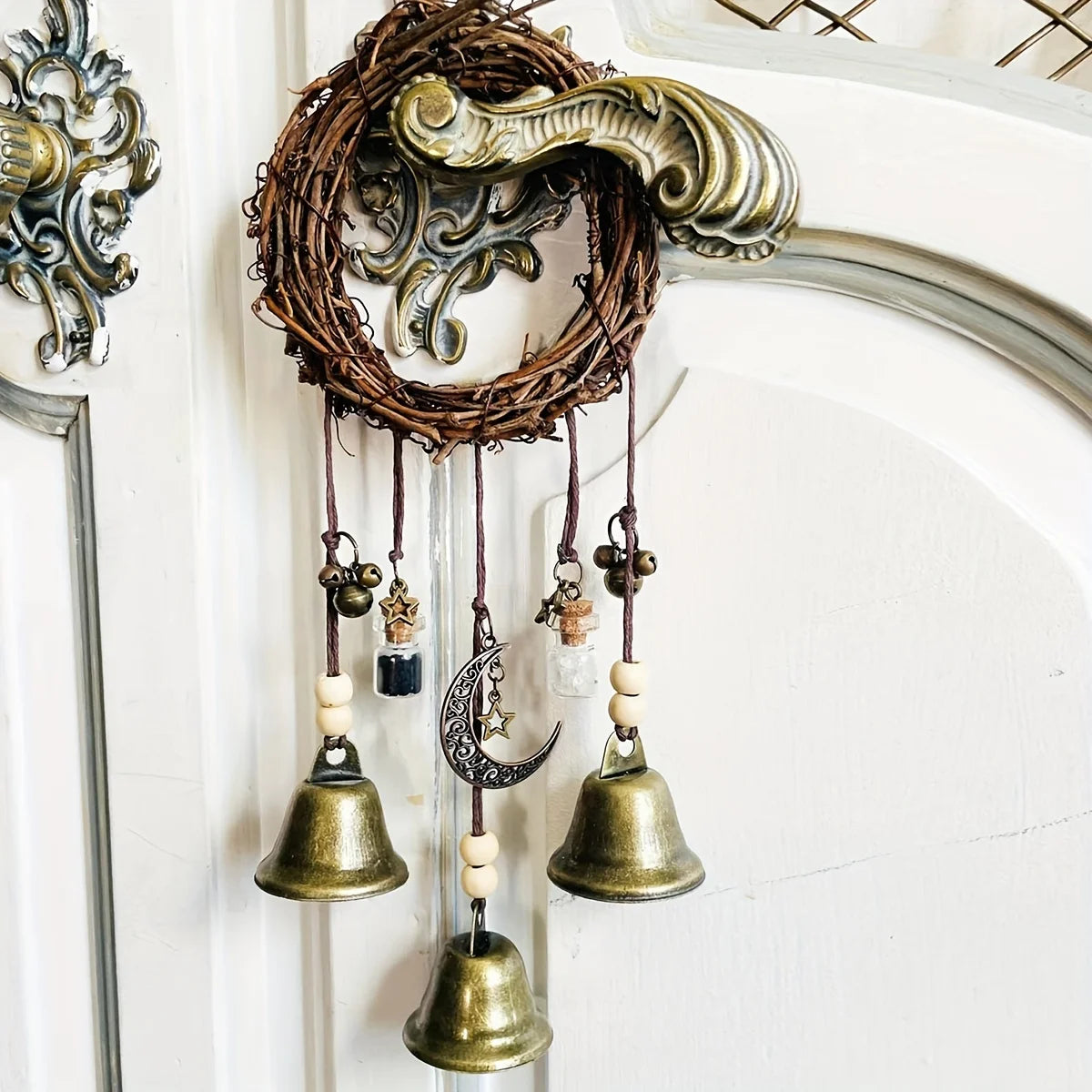 A vintage wicker wreath with hanging brass bells and charms displayed on a white door.