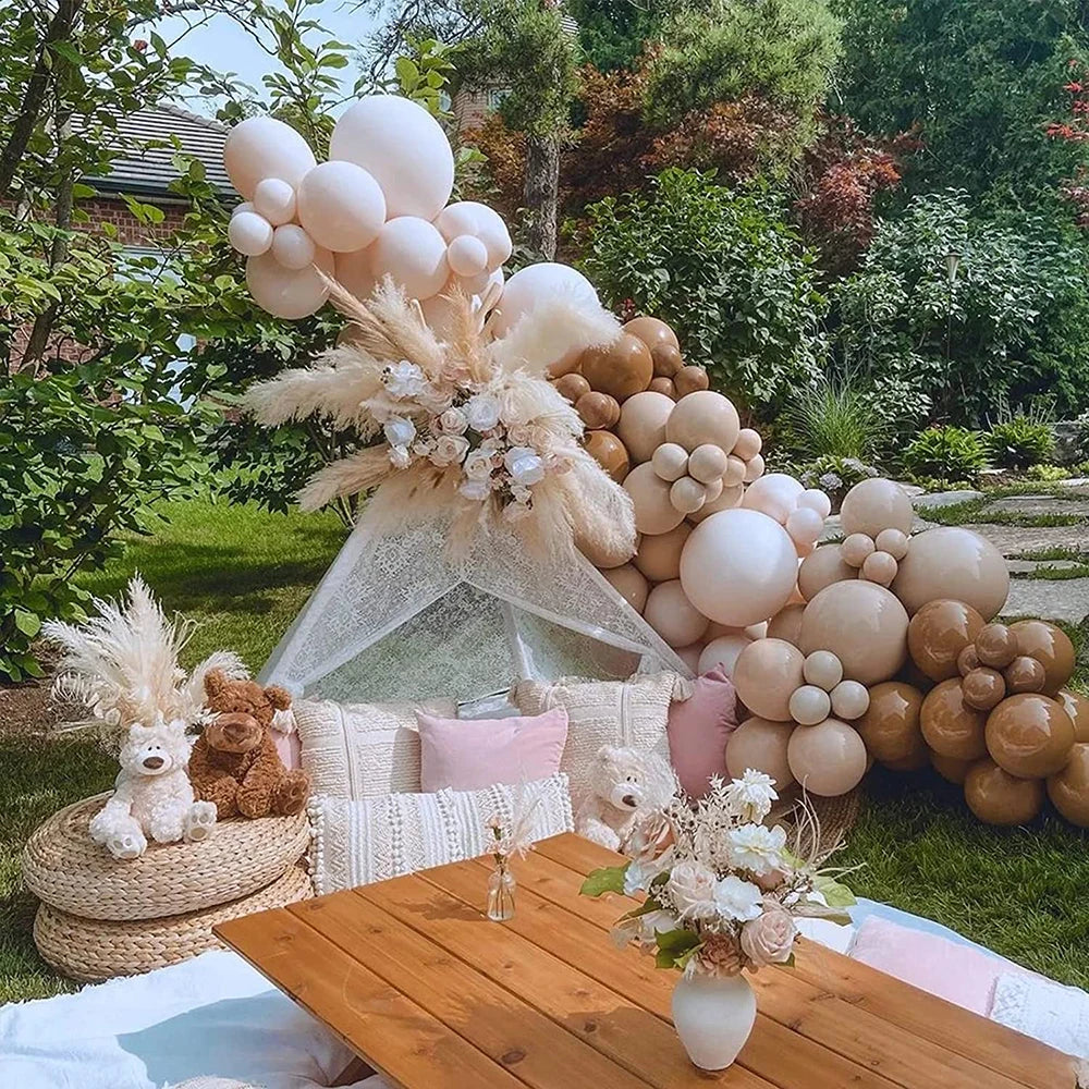 A display of elegant sand white latex balloons and dried floral arrangements set on a wooden table outdoors.