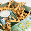 Grüne Box mit zerknülltem braunem Papier-Füllmaterial und dekorativem Deckeldesign.