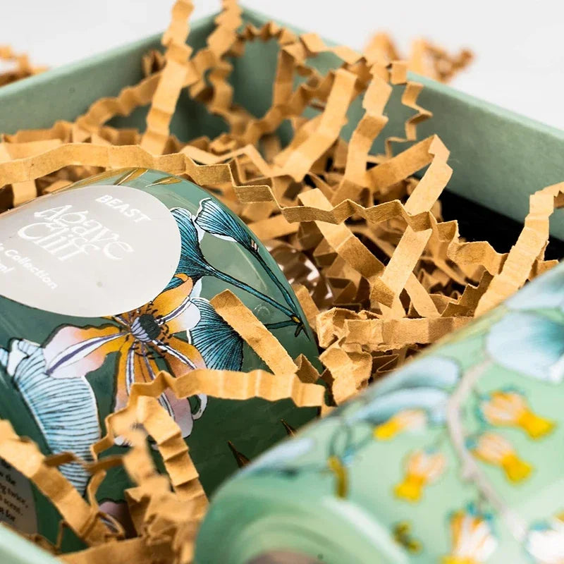 Grüne Box mit zerknülltem braunem Papier-Füllmaterial und dekorativem Deckeldesign.
