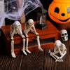 A set of three white resin skeleton skull figurines displayed on a wooden box next to a glowing jack-o'-lantern.