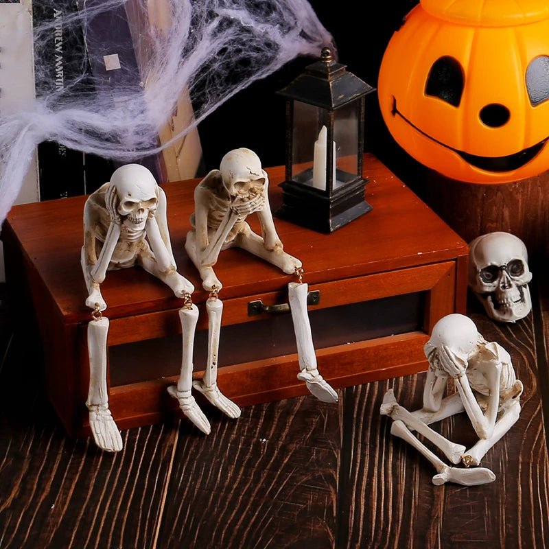 A set of three white resin skeleton skull figurines displayed on a wooden box next to a glowing jack-o'-lantern.