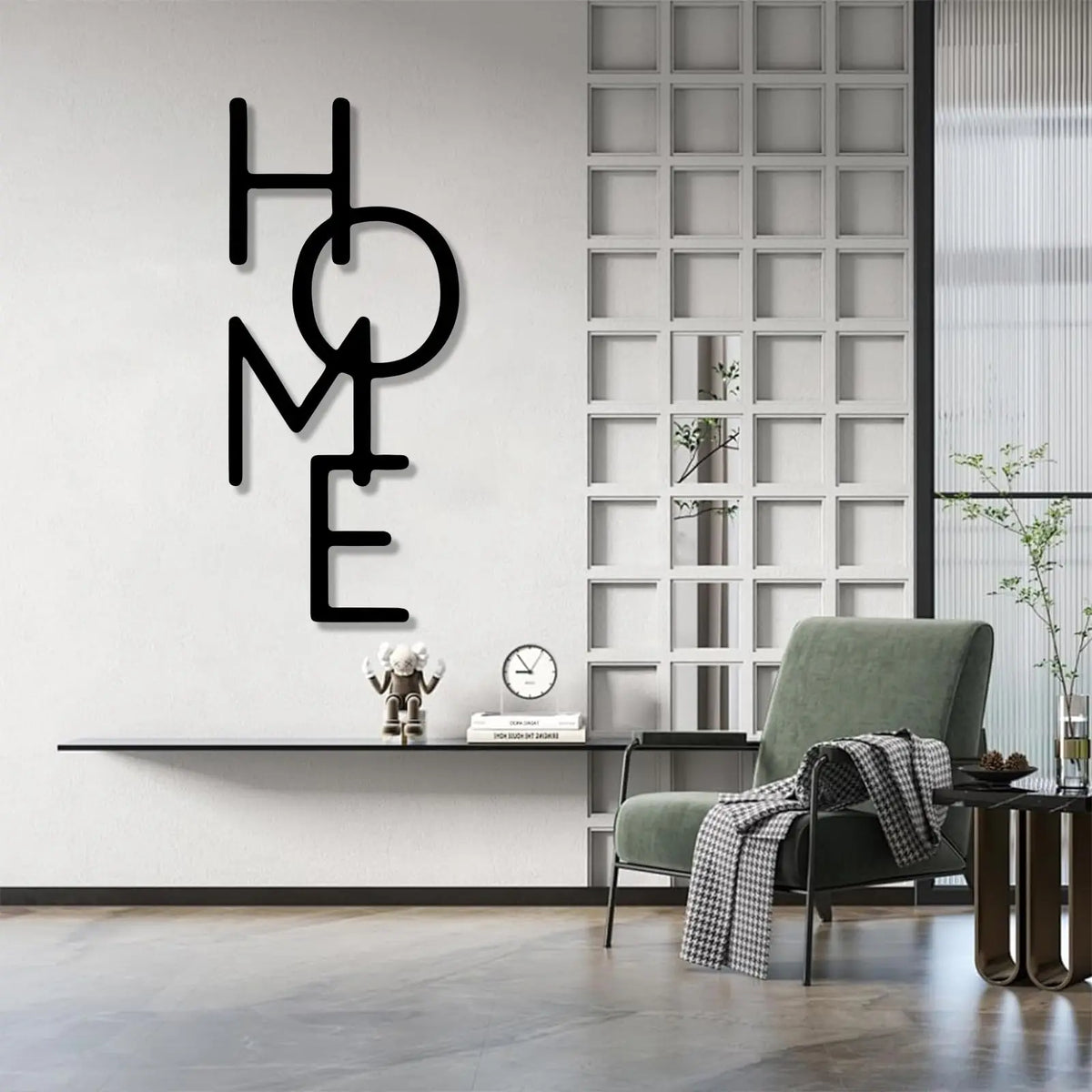 Black metal word art spelling HOME mounted on a white wall with a glass grid partition and a green armchair.