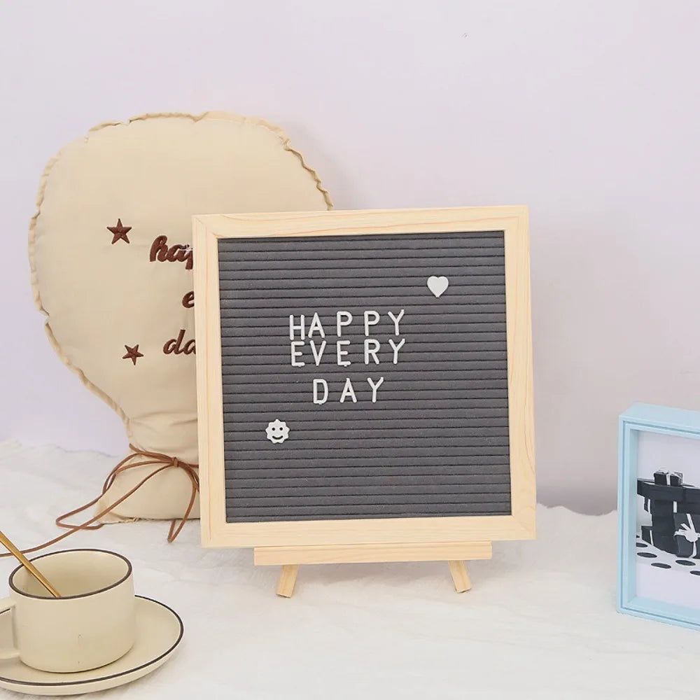A wooden message board with a gray grid displaying HAPPY EVERY DAY and a small heart, next to a light beige decorative item.
