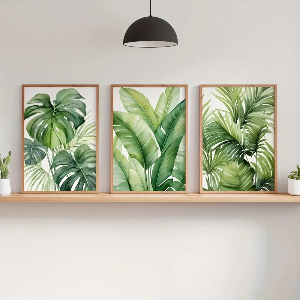 A set of three watercolor leaf art prints featuring lush green tropical leaves displayed on a wooden shelf.