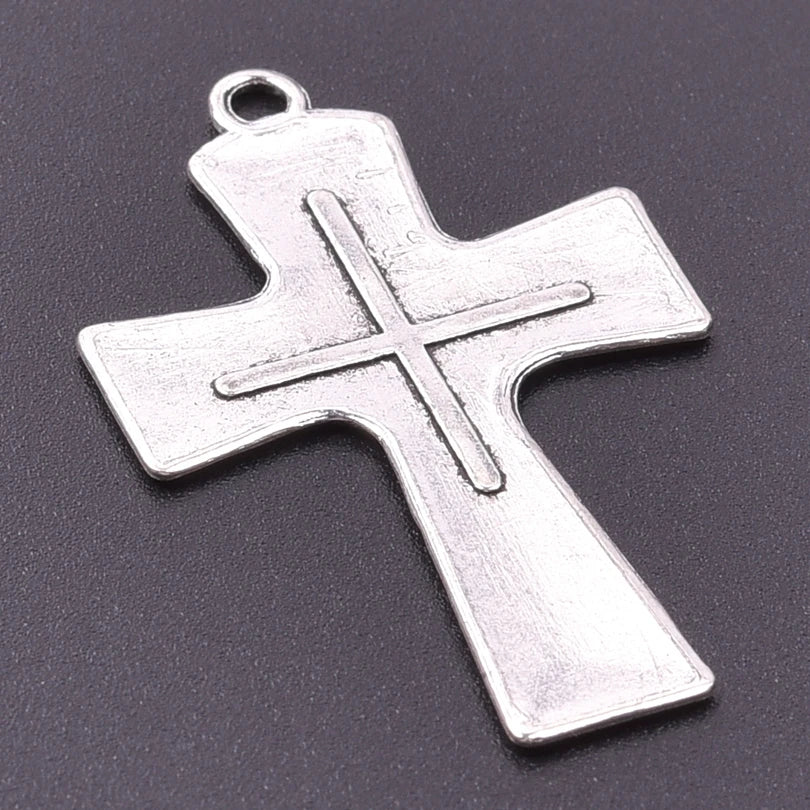 A silver antique cross charm with a bail, displayed against a dark gray background.