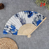 A hand carved bamboo folding fan with blue and gray floral patterns displayed on a gray surface.