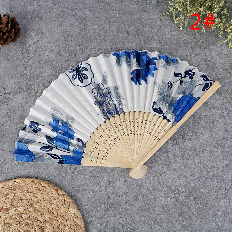 A hand carved bamboo folding fan with blue and gray floral patterns displayed on a gray surface.