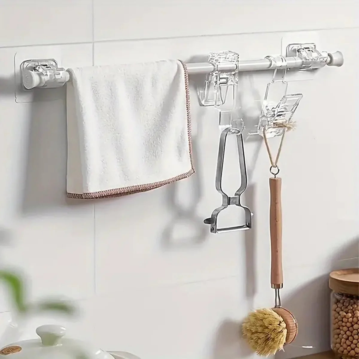 Silver self-adhesive curtain rod holders with various hooks and a wooden hanger mounted on a white wall.