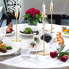 A table setting featuring three gold metal taper candle holders with white candles and various food dishes.