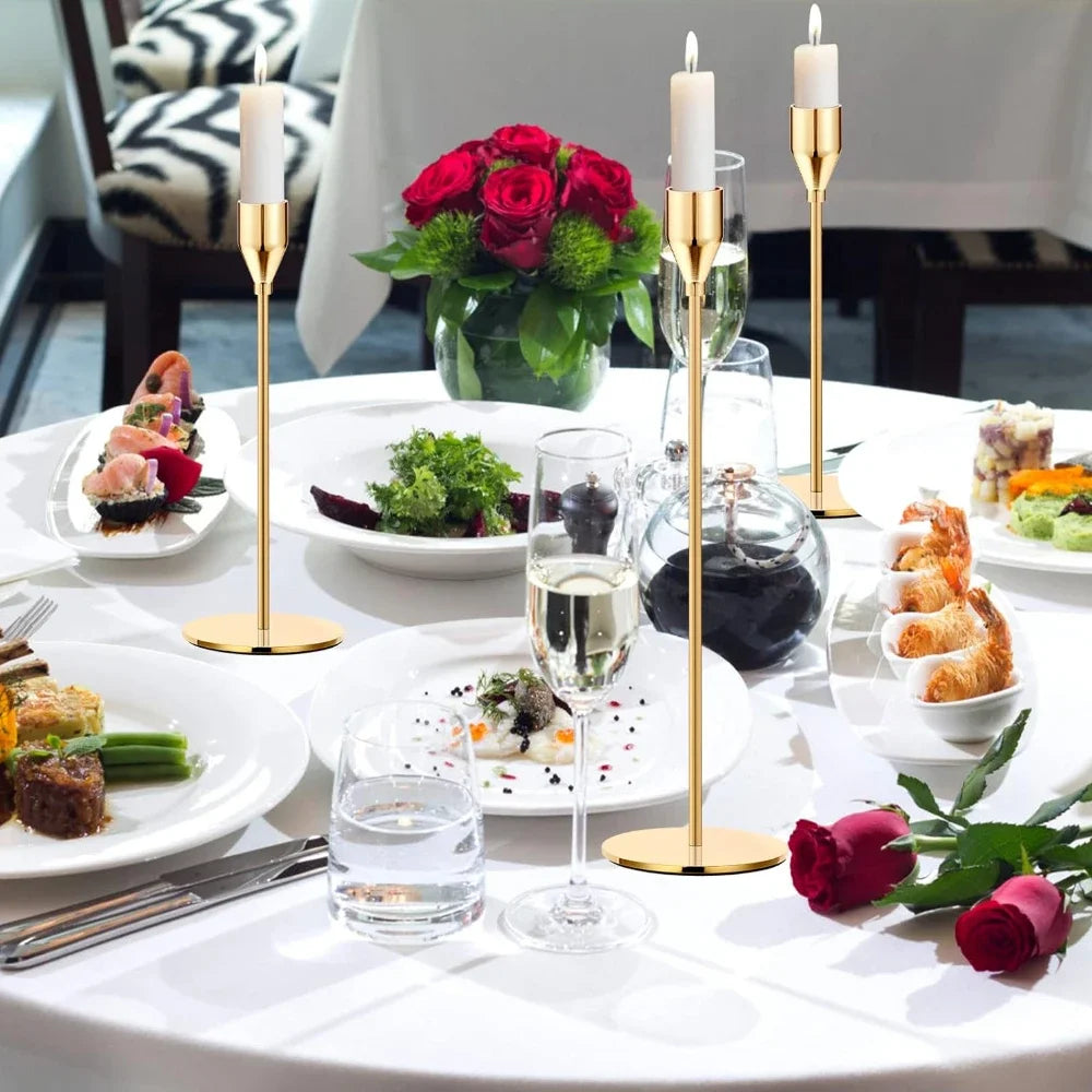 A table setting featuring three gold metal taper candle holders with white candles and various food dishes.