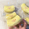 A hand holds a yellow squishy toy shaped like a banana bear, packaged in clear plastic.