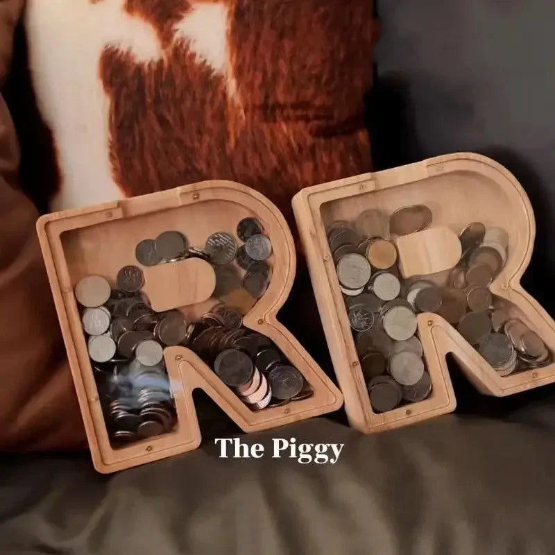 A wooden alphabet piggy bank box filled with various coins, resting on a brown fabric.
