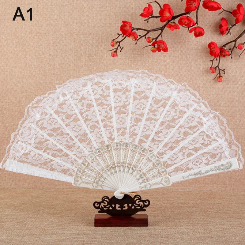 A white lace folding hand fan with a decorative base is displayed against a background of red blossoms.