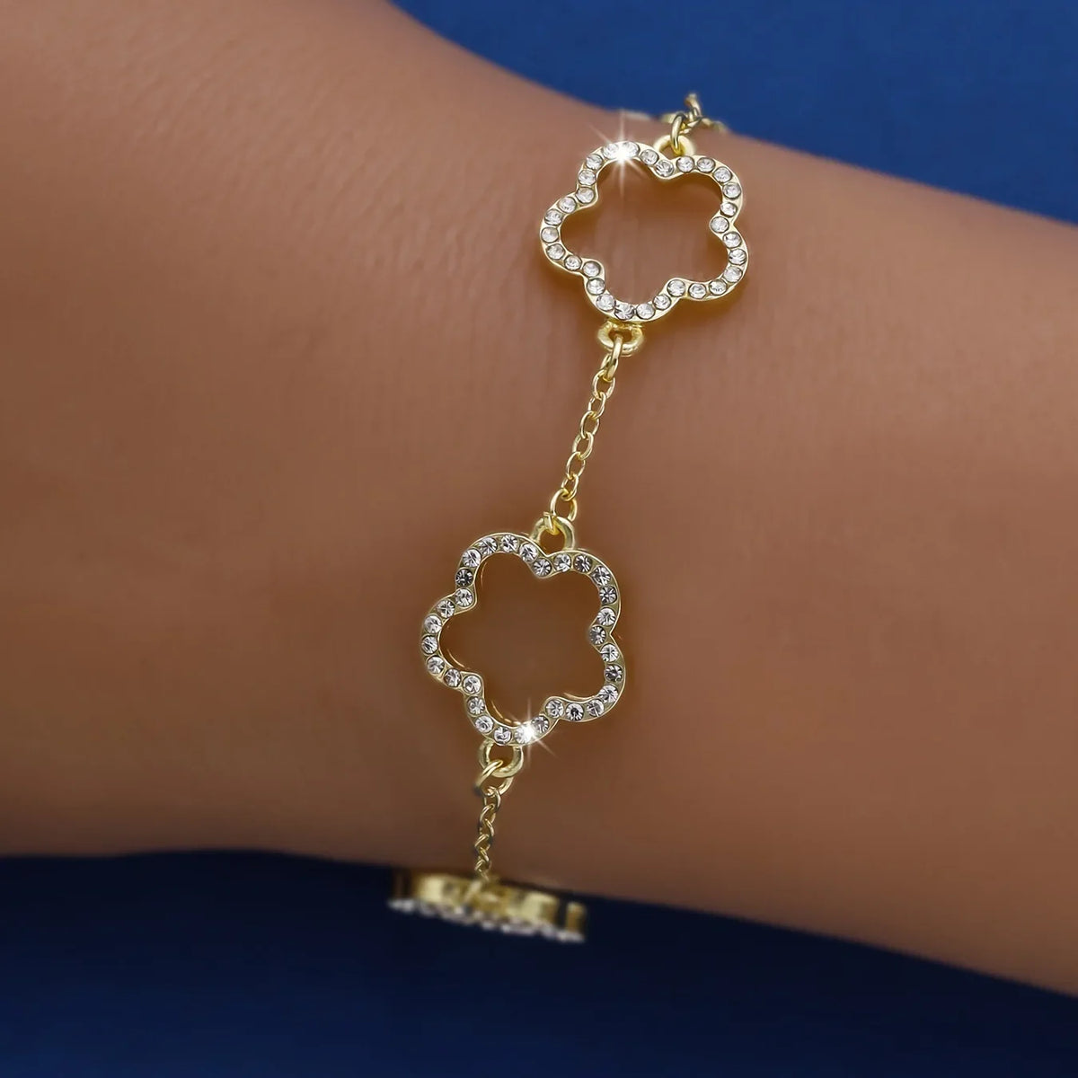 A gold-plated cubic zirconia flower bracelet is worn on a person's wrist.
