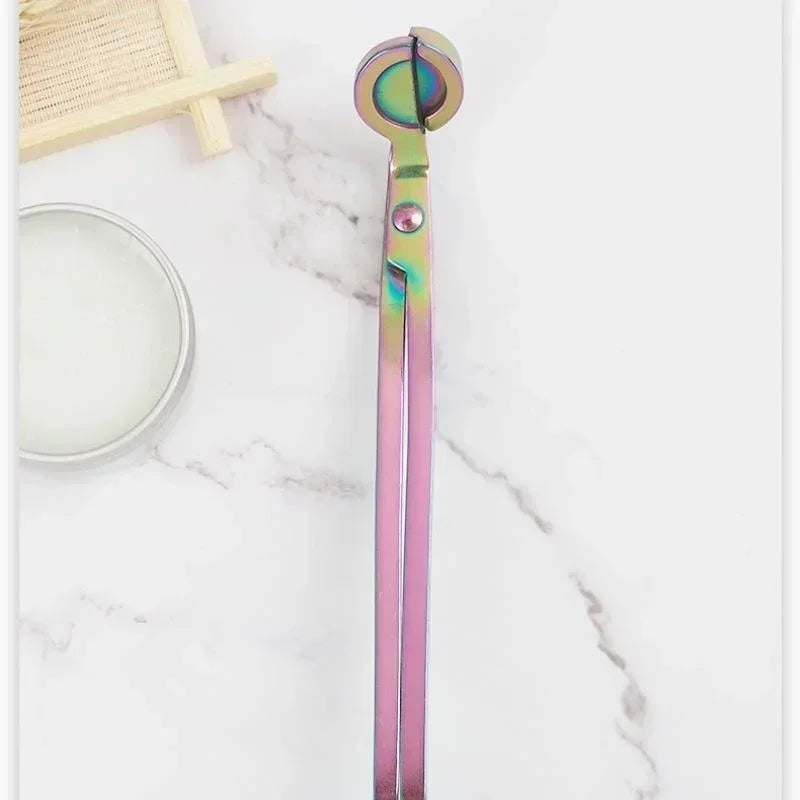 A pair of iridescent pink and green stainless steel candle wick trimmer scissors resting on a white marble surface.