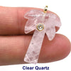 A clear quartz pendant shaped like a palm frond with a zircon charm, held by a finger.
