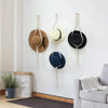 A set of macrame hat organizers featuring wooden dowels and various sized hats hanging on a white wall.