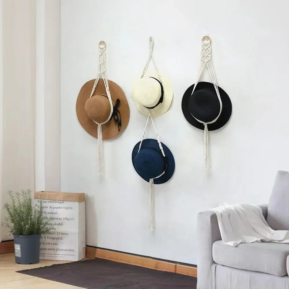 A set of macrame hat organizers featuring wooden dowels and various sized hats hanging on a white wall.