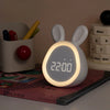 A white mini LED cartoon rabbit night light alarm clock displaying 22:00 on a wooden surface.