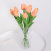 A bouquet of artificial peach-colored tulips in a clear glass vase