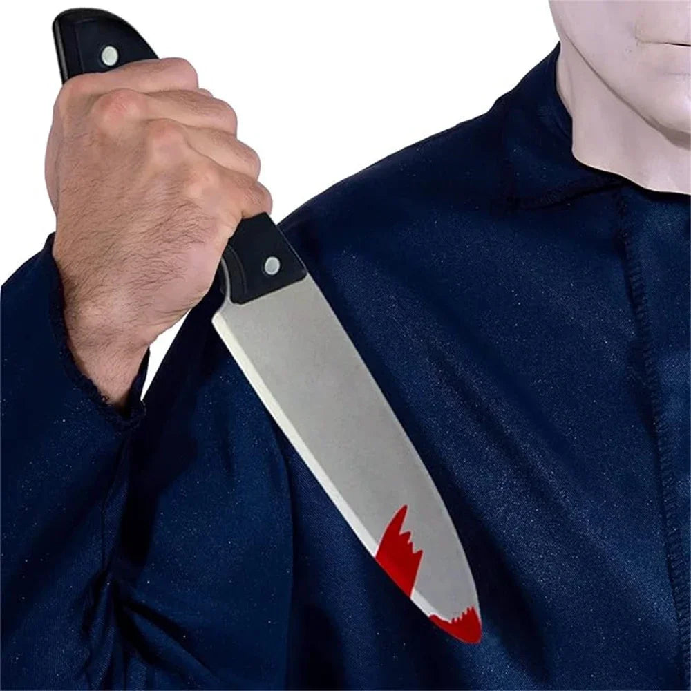 A hand holds a realistic bloody knife prop against a dark blue shirt.