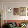 A rustic wooden wall clock with a white face and Roman numerals hangs on a light gray wall above a green sofa.