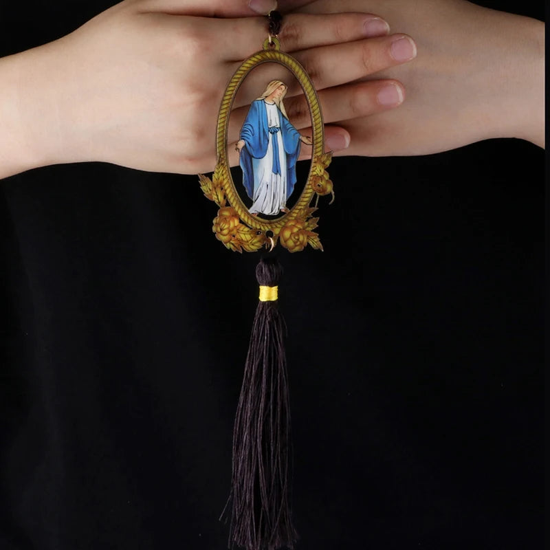 A wooden pendant ornament depicting Our Lady of Grace with a blue and white robe, held by a person's hand.