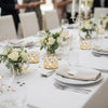 A white table setting for an event featuring crystal gold votive candle holders and floral arrangements.