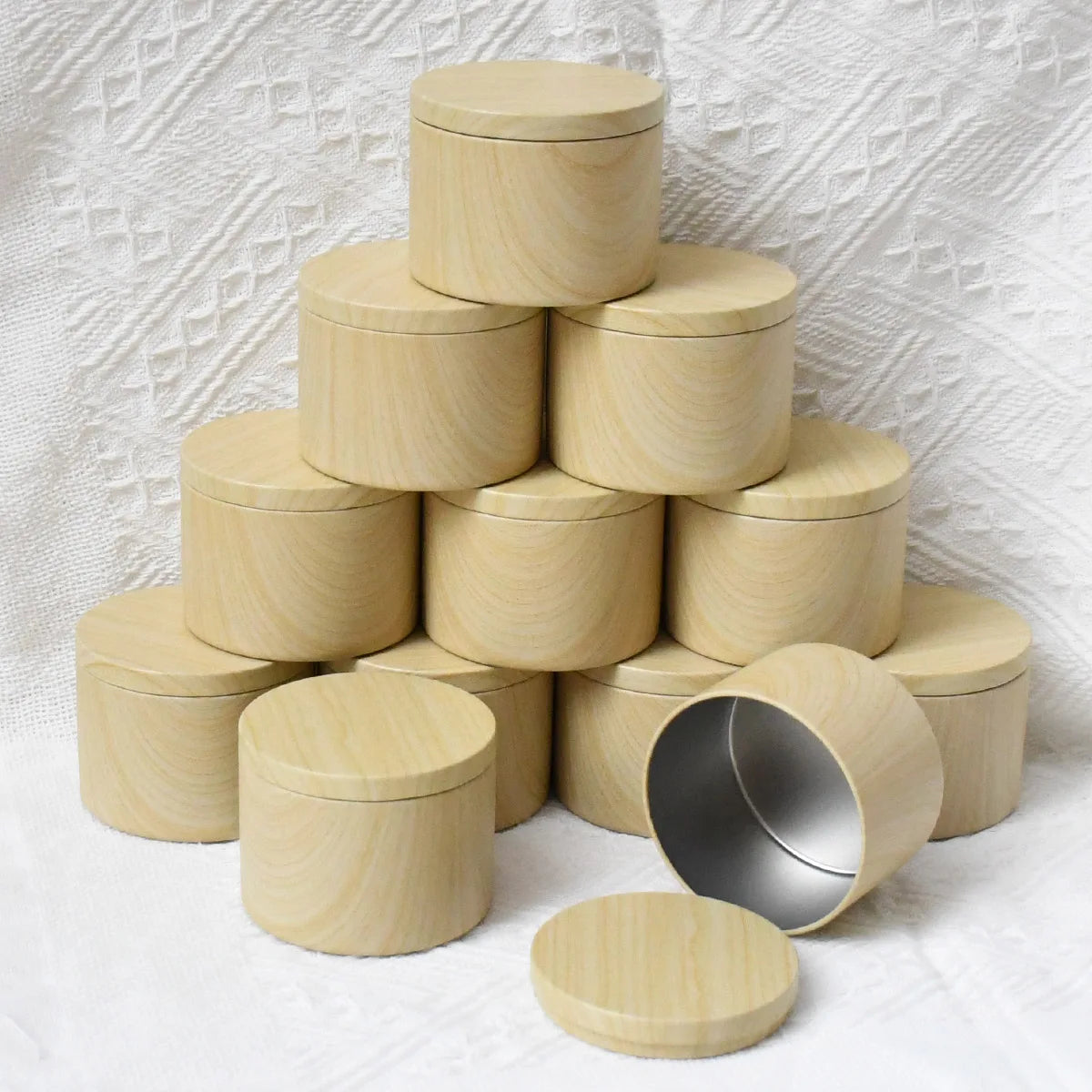 A stack of light wood metal candle tins with lids arranged in a pyramid shape.
