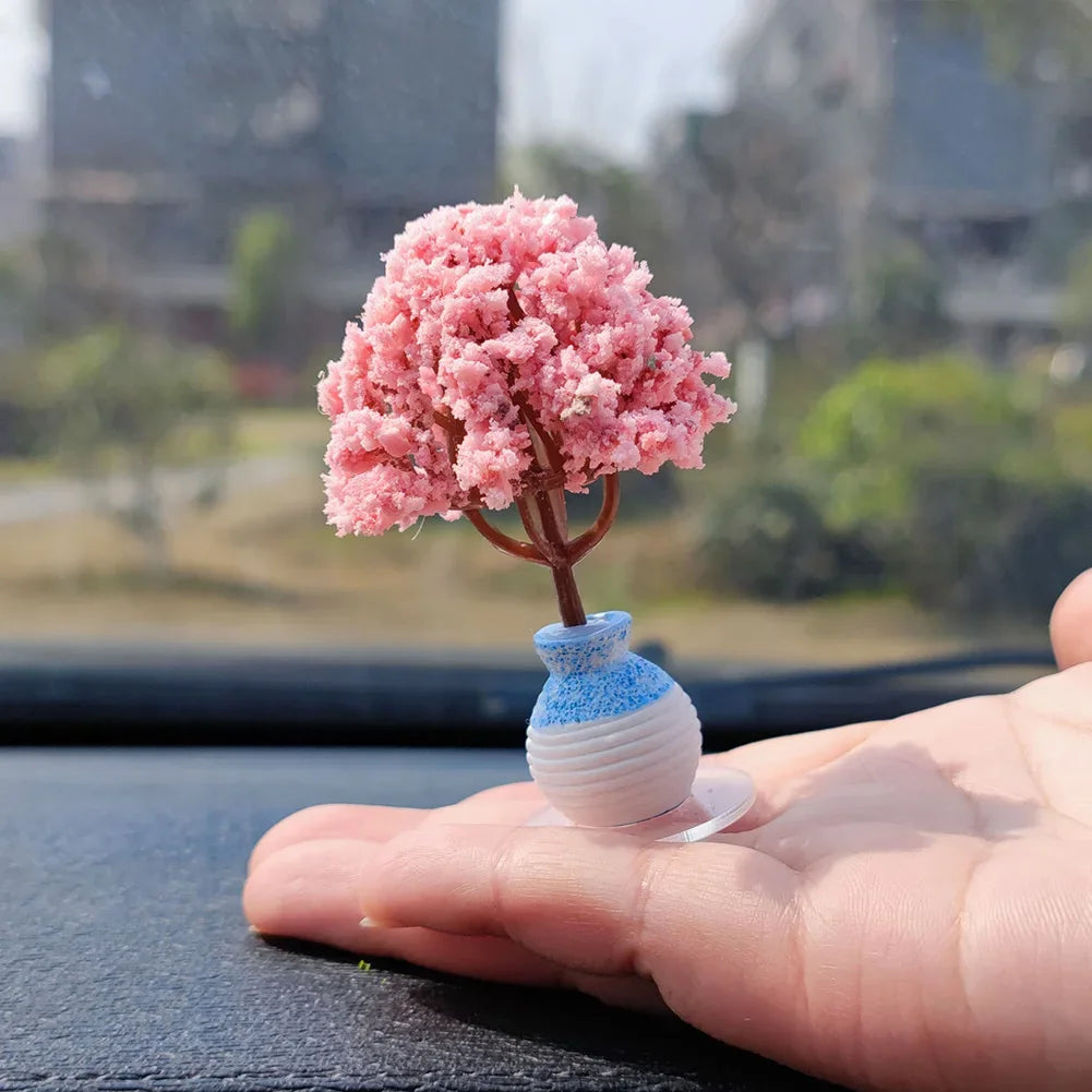 A small, pink, flowering tree ornament sits on a blue and white glass bottle in the palm of a hand.