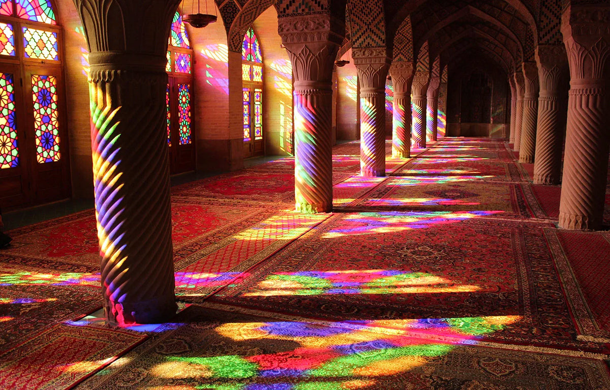 Interior view of an Islamic mosque with arched columns and colorful light patterns cast on the floor.