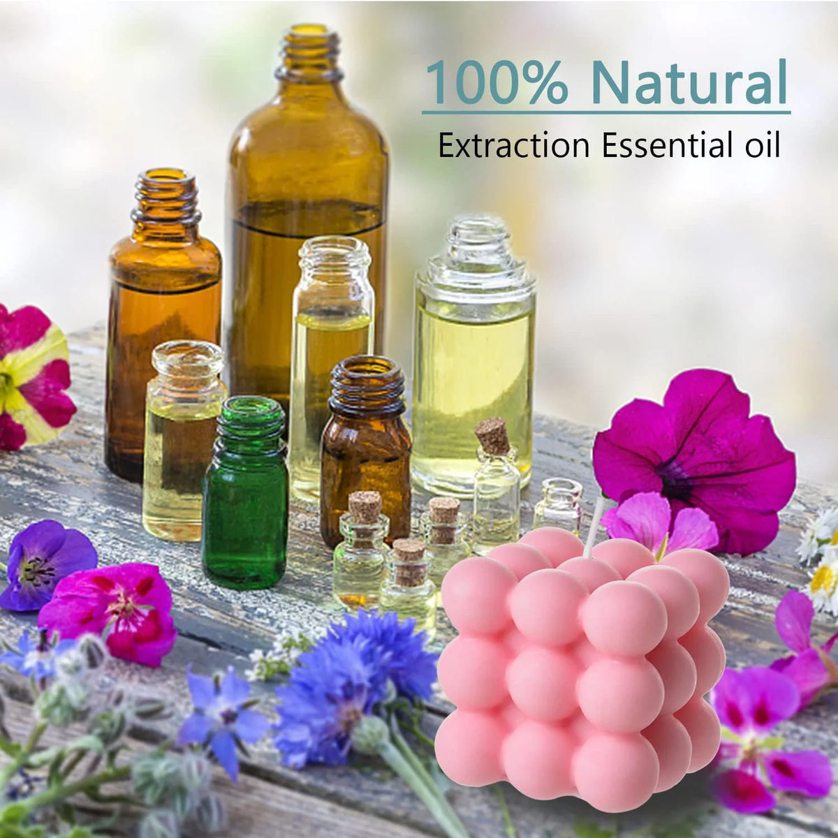 A collection of essential oils in glass bottles and pink wax candles surrounded by colorful flowers and greenery.