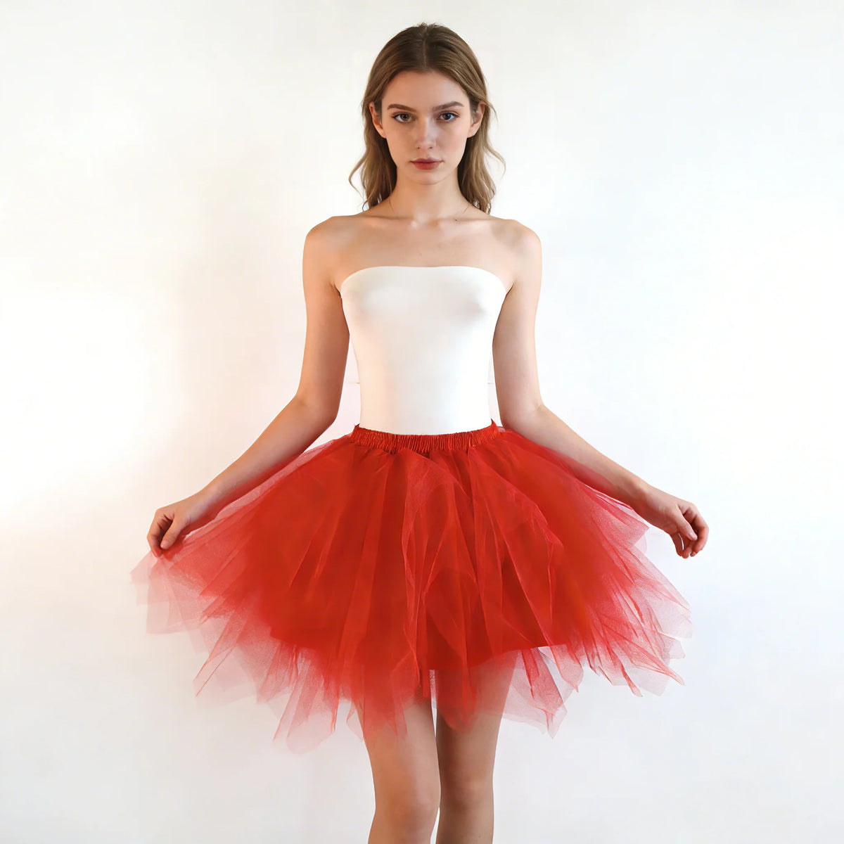 A woman models a strapless white bodice and a voluminous red tulle tutu skirt against a white background.