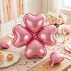 A set of ten pink heart-shaped foil balloons arranged on a wooden surface with floral decor.