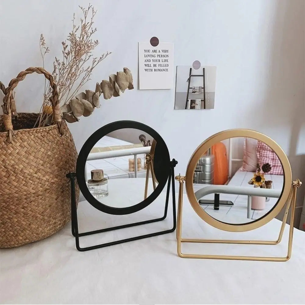 A set of two circular metal makeup mirrors, one black and one gold, displayed on a white surface.