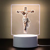 A 3D LED night light displays a crucifix with a figure of Jesus on a light background.
