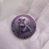 A silver coin featuring a moon rider design on a purple background held in a white glove.