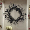 An artificial black branch bat wreath for Halloween door decor hangs on a white door.
