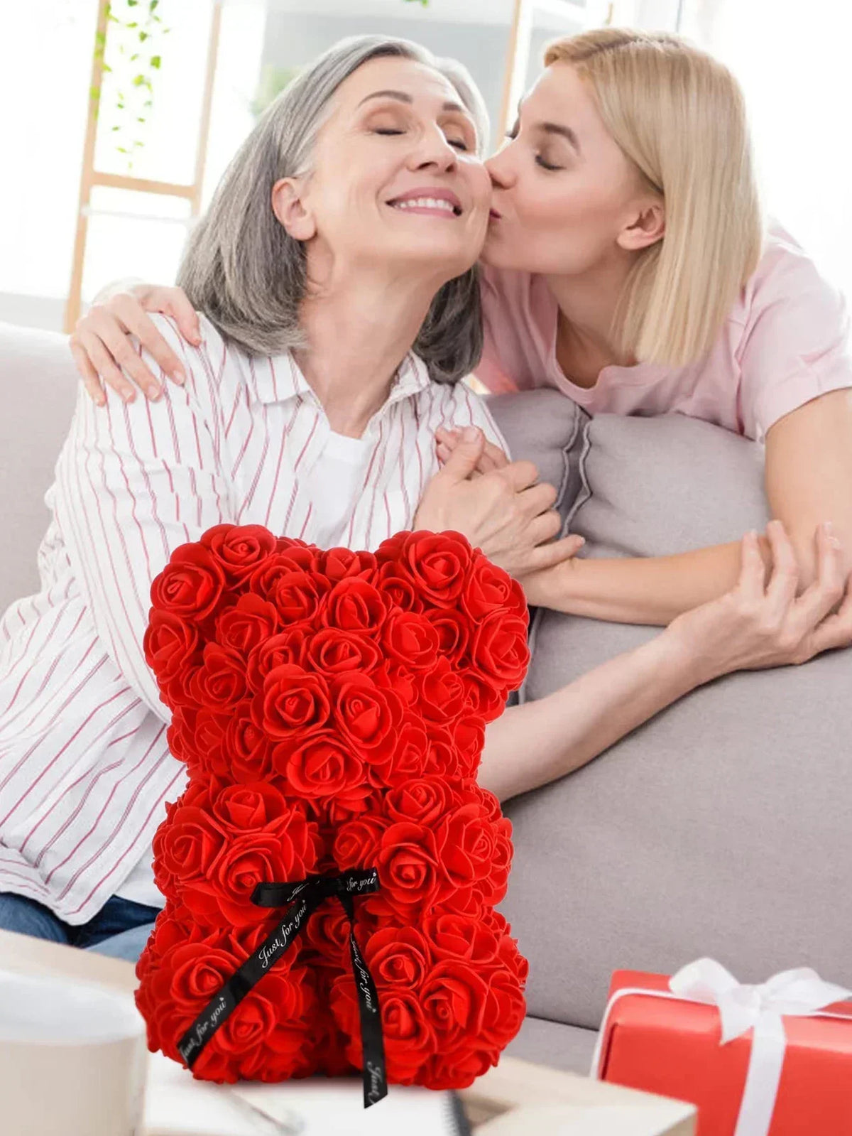 Ein leuchtend roter künstlicher Rosen-Teddybär auf einem Tisch vor zwei Frauen.