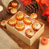 A wooden box filled with golden orange pumpkin hanging ornaments surrounded by autumn leaves and pine cones.