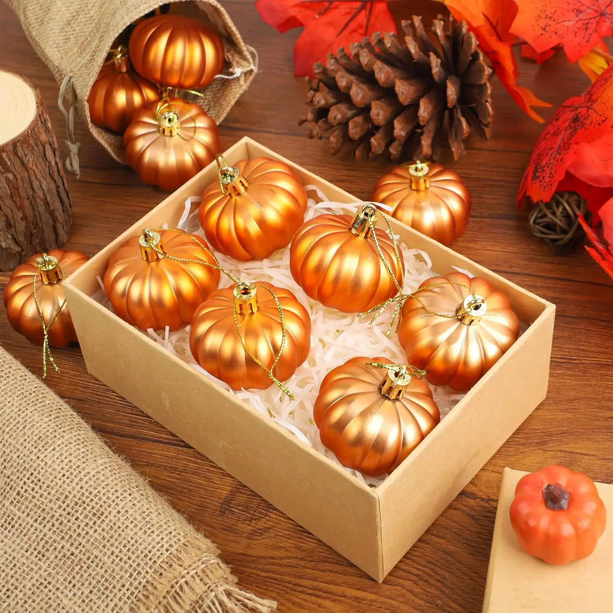 A wooden box filled with golden orange pumpkin hanging ornaments surrounded by autumn leaves and pine cones.
