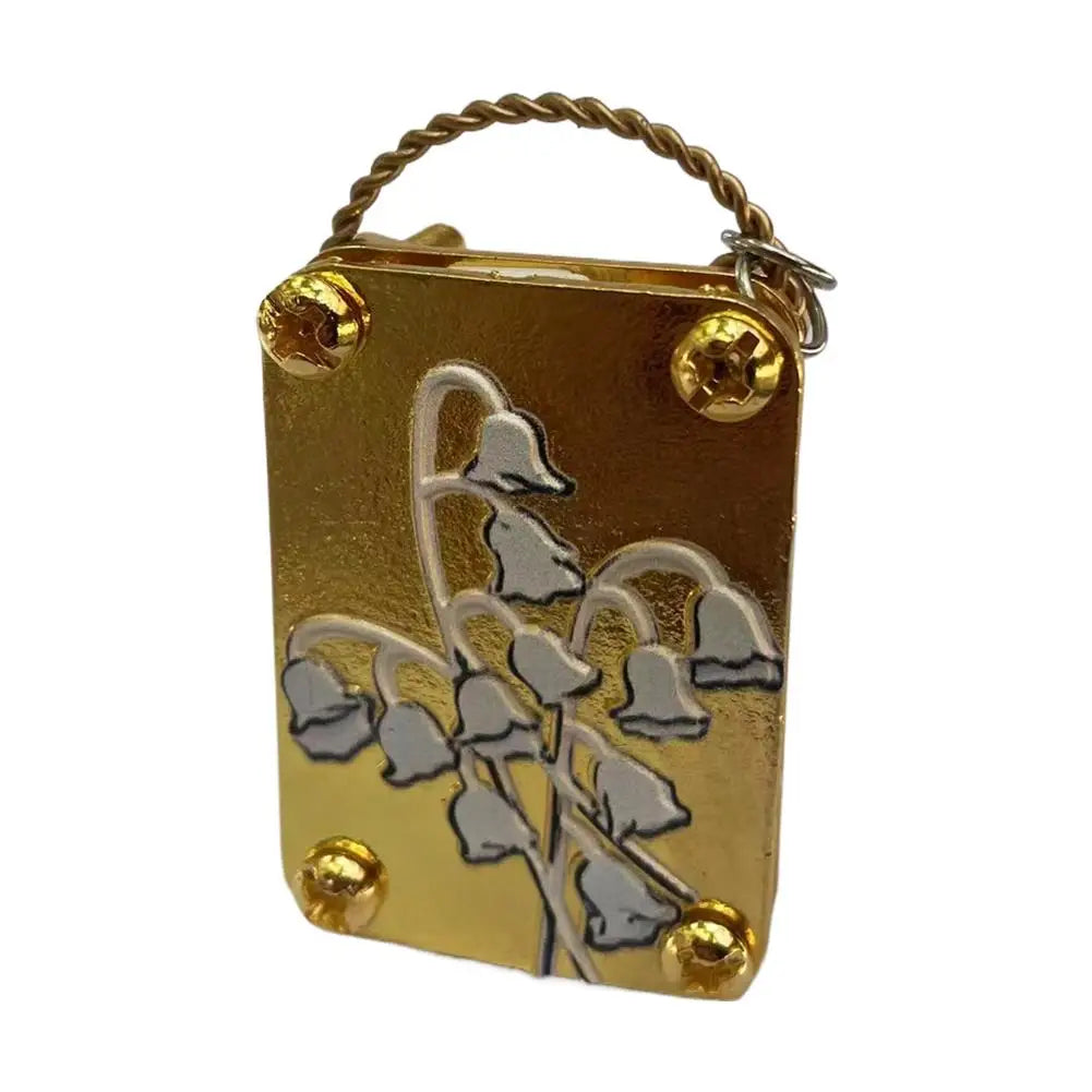 A small brass metal box with a wire loop, featuring an engraved design of white flowers.