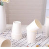 A collection of white disposable paper cups arranged on a checkered surface with a vase of flowers in the background.