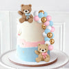 A tiered cake decorated with teddy bear toppers and pastel blue, pink, and gold balloons for a gender reveal party.