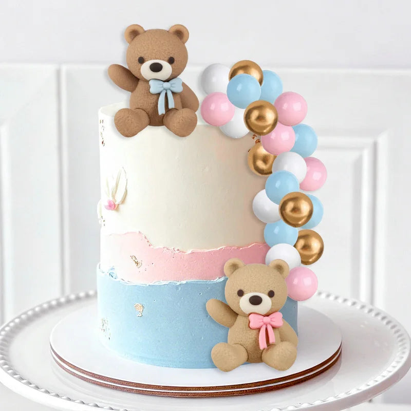 A tiered cake decorated with teddy bear toppers and pastel blue, pink, and gold balloons for a gender reveal party.