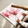 A watercolor illustration of pink and magenta lotus flowers on a white poster, next to a rolled canvas.