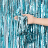A hand is holding and manipulating blue metallic foil fringe curtain strands.